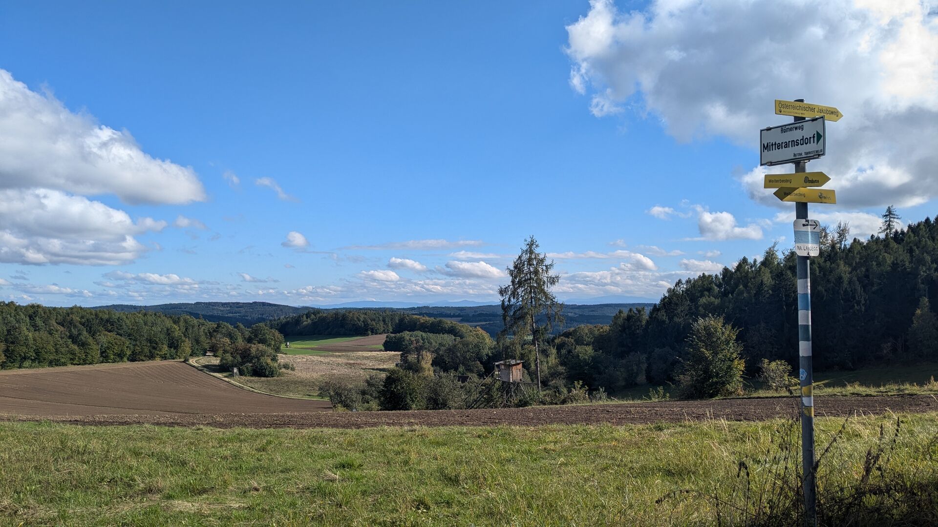 Aussicht auf Schenkenbrunn und Dunkelsteinerwald von Kreuzberg. Wandertafel mit Richtungspfeilen.